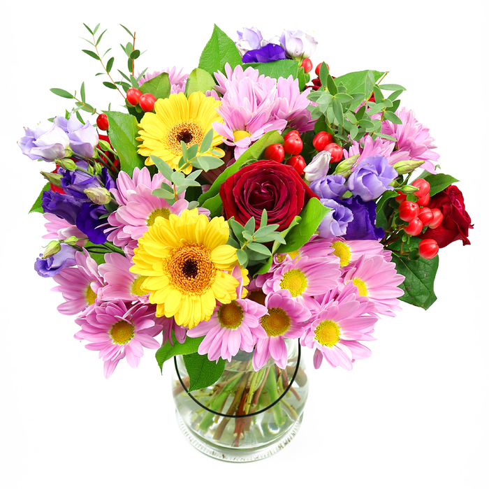 A generously sized mixed bouquet bursts from a clear glass vase in this photograph, the pristine white background allowing its rich colours to shine. In the centre, luxurious red roses with soft, velvety petals create a core of depth and sentiment, reminiscent of traditional romance. Around them, clouds of pink and lavender daisies or chrysanthemums form a gentle collar, each bloom featuring multiple slender petals that frame a bright yellow centre, giving a cushiony, almost feather-light effect. Two striking yellow gerbera daisies with dark brown-orange centres break through the pastels, infusing the arrangement with an upbeat, sunlit energy that would brighten any Luton home. Slender purple and lilac lisianthus stems, bearing graceful bell-shaped flowers and buds, move through the design like painted brushstrokes, adding a cool, elegant dimension and soft vertical lines. Nestled between the petals are glossy red hypericum berries, their round form adding playful texture and a hint of festive charm. A mix of rich green foliage-from broad, darker leaves that provide structure to finer, lighter green sprigs that add lightness-cradles the flowers, making the bouquet feel lush and well balanced, as though freshly gathered from a local Bedfordshire garden. The glass vase reveals the tidy stems arranged in clear water, showcasing the florist's attention to detail and care. The arrangement evokes a feeling of celebration and warmth, perfect as a birthday surprise in Wigmore, a thank-you delivered to a friend in Farley Hill, or a colourful centrepiece that brings life to a dining table near Wardown Park. It feels like a thoughtful creation from a local Luton florist who understands how to blend colour, texture, and emotion.
