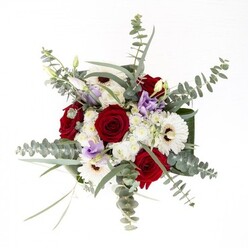 As a florist devoted to the Luton community, arranging this bouquet feels like composing a local symphony-each flower adding its own note yet harmonising into a whole. The intense, velveteen reds of the classic roses speak to enduring affection, their forms unfurling like the historic pages of Luton's story. Crisp white gerberas with their bold brown eyes provide structure and brightness, much like the pillars of St. Mary's Church. Slender eucalyptus leaves arc overhead, imparting both movement and a bracing aroma reminiscent of open skies at Wardown Park's arboretum. Lavender lisianthus, in both blossom and tight bud, scatter through the arrangement, their color breathing a touch of modernity among traditions. Fluffy white filler flowers lend a softness found in Luton's wild meadows, while broad, emerald-green leaves frame the base with substance. Every stem, visible through the crystal vase and immersed in clear water, speaks of freshness and careful curation. This composition is at home gracing a Bury Park celebration or bringing comfort to a neighbour-the mark of a true Luton florist's intention: to blend artistry, beauty, and the seasons of our town.