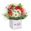 There's an effortless cheerfulness in this bouquet, nestled gracefully in its pristine white square gift bag, that seems to channel the positive energy found throughout Luton's bustling markets and friendly neighbourhoods. Billowing coral and peach carnations, soft and abundant, radiate with uplifting colour, while lively white daisies with gleaming yellow-green centres offer a sense of lighthearted joy. Wisps of baby's breath drift through the bouquet, brightening it with a dreamy, cloudlike air. A hint of unopened, purple-tinged buds adds a playful touch of anticipation along one side. Framed in rich green foliage-each leaf glossy and robust like those seen along Luton's leafy avenues-the arrangement is carefully shaped into a rounded mound that feels at once modern and heartfelt. The white bag, topped by neat ribbon handles, transforms the bouquet into a ready-to-give gesture, whether marking a new chapter, offering birthday wishes, or simply sending a thoughtful surprise. Every flower and leaf has been placed with mindful expertise, ensuring both freshness and local authenticity. Lit gently to showcase the interplay of vibrant and soft tones, the whole impression is one of genuine warmth and celebration-a bouquet that truly brings the heart of Luton straight to your doorstep.