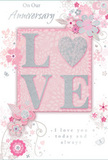 This anniversary card presents a gentle celebration of enduring romance, captured in soft pastel pinks and cool silvery greys that would feel perfectly at home in a cosy Luton living room. At the centre, the word LOVE is spelled out in raised, softly glittering letters, each stroke shimmering with blush tones and fine silver highlights. The letter O becomes a shimmering heart, richly textured in silver glitter, giving the design a focal point that is both playful and deeply affectionate. Behind the word lies a smooth blush-pink panel, its hue reminiscent of early cherry blossoms in Wardown Park, providing warmth against the paler outer background. Around this central motif, delicate blooms unfurl in blush, mauve, and gentle ivory, painted with a near-watercolour softness that lets colours bleed into one another. Slender stems and swirling vines curl around the flowers, traced in fine lines that suggest movement and care, like the thoughtful gestures that sustain a long relationship. Tiny flourishes-loose petals, looping scrolls, and a scattering of almost-transparent butterflies-add motion and a hint of whimsy, evoking the lightness of an English spring garden. Above and below, the phrases On Our Anniversary and I love you today and always are rendered in an understated, elegant script that harmonises with the flowing floral shapes. The overall impression is intimate and heartfelt, a paper companion to an anniversary bouquet delivered across Luton by Flower Delivery Luton, perfect for marking a shared journey that is as soft-spoken as it is deeply rooted in love.